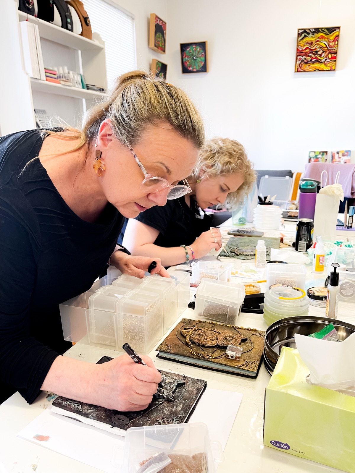 Two participants leaning into focused, detailed work at the studio table